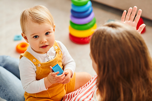 A baby girl and her mother interact, playing joyfully on the floor at home.