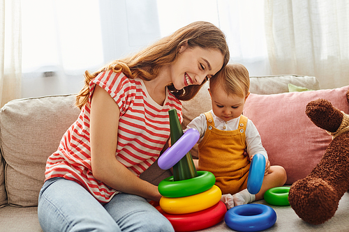 A young mother and her toddler daughter laughing and playing on a cozy couch, creating precious memories together.