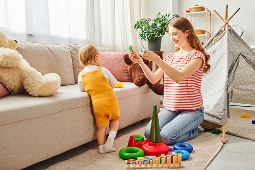 A young mother and her toddler daughter laughing and playing in a warm and inviting living room.