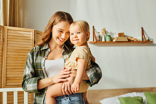 A young mother lovingly cradles her toddler daughter in her arms, creating a tender moment of connection and affection at home.