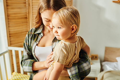 A young mother lovingly holds her small daughter in her arms at home, creating a heartwarming moment of connection.