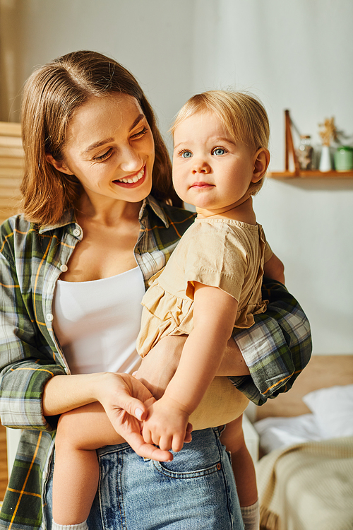 A young mother cradles her toddler daughter in her arms, sharing a moment of love and connection at home.