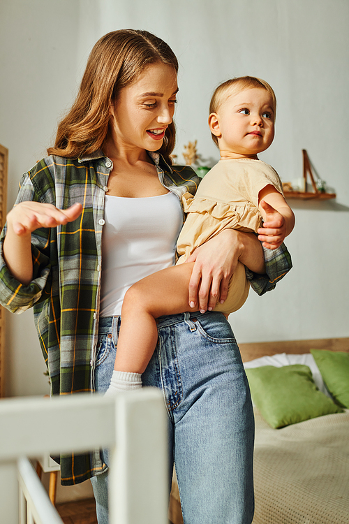 A young mother lovingly holds her toddler daughter in her arms, sharing a moment of bonding and affection at home.