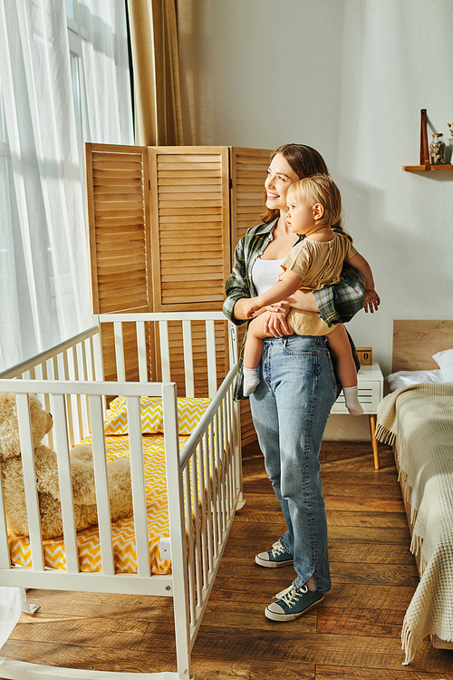 A young mother lovingly cradles her baby daughter in a white crib, creating a heartwarming scene of maternal care and bonding.