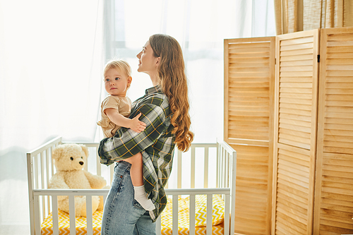 A young mother lovingly holds her baby daughter in her arms, sharing a moment of warmth and closeness at home.