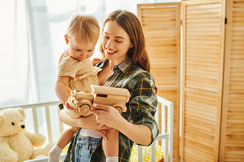 A young mother tenderly holds her toddler daughter in her arms, expressing love and affection in a cozy home setting.