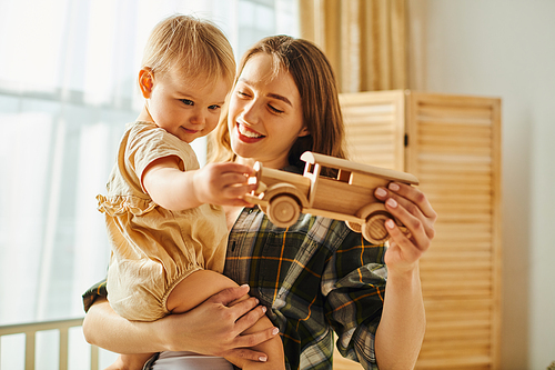 A young mother holds her baby girl while they play with a toy car, bonding and creating cherished memories at home.