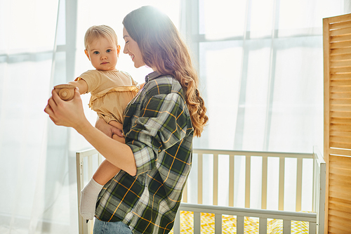 A young mother lovingly holds her toddler daughter in her arms, sharing a heartwarming moment of bonding and affection at home.