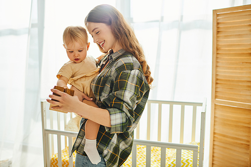 A young mother tenderly holds her toddler daughter in her arms, sharing a heartwarming moment of love and connection at home.