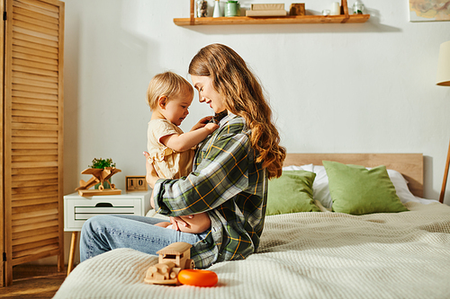 A young mother sits on a bed, cradling her baby daughter in her arms, sharing a moment of love and tenderness.