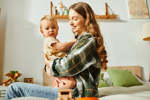 A young mother sitting on a bed, gently holding her baby daughter in her arms, cherishing a precious moment together.