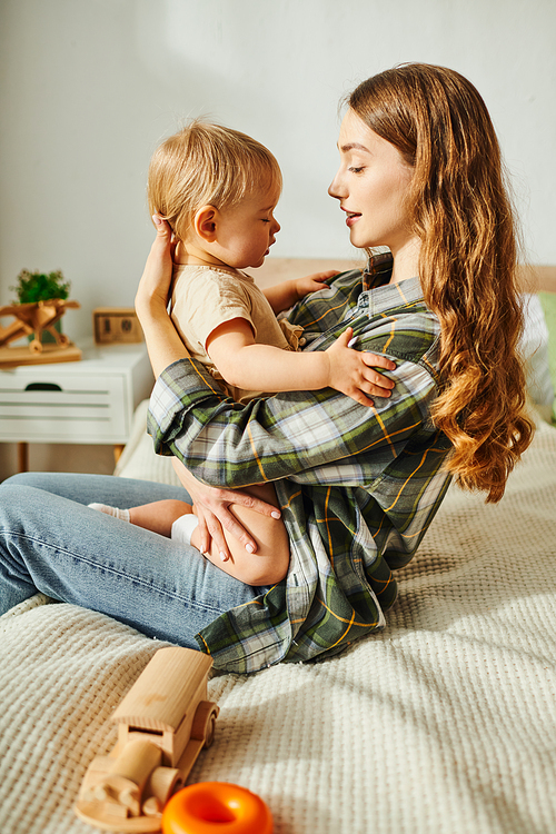 A young mother sits on a bed, lovingly holding her small child, creating a warm and intimate moment between them.