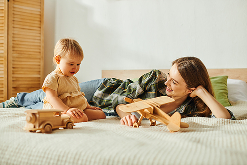 A young mother lays on a bed next to her toddler daughter, sharing a serene and heartwarming moment of bonding.