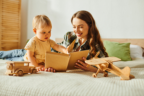 A young mother reads a book to her toddler daughter, creating a magical moment of love and connection on a cozy bed.