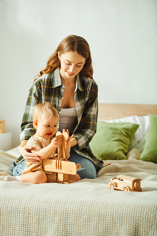 A young mother joyfully plays with her toddler daughter on a cozy bed, creating heartwarming memories together.