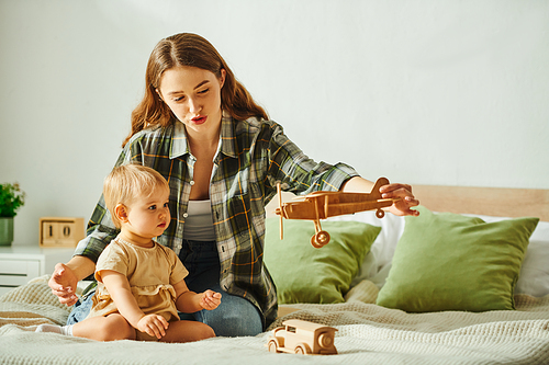 Young mother lovingly plays with her toddler daughter on a cozy bed, creating joyful and memorable family moments.