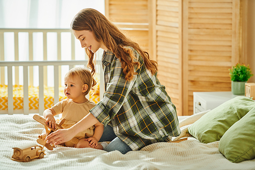 Young mother sitting on a bed next to her baby daughter, sharing a moment of love and connection in a cozy home setting.