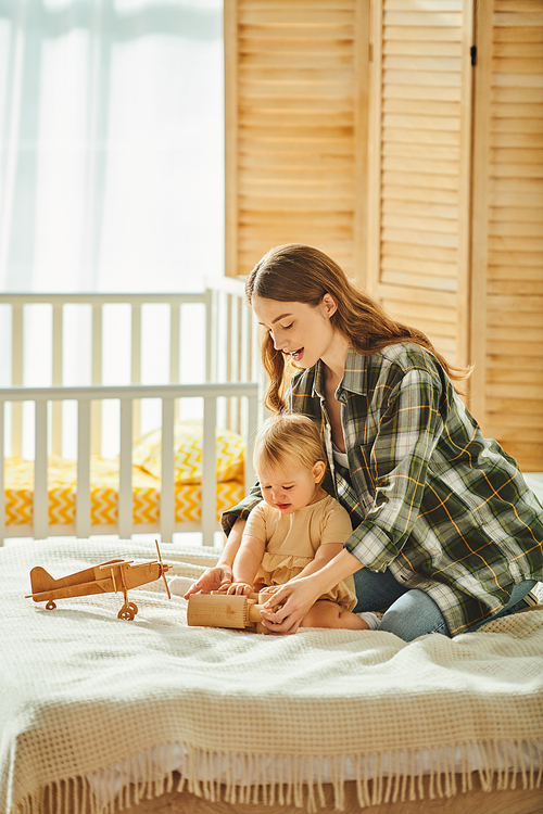 A young mother sitting on a bed next to her baby daughter, sharing a special moment together at home.