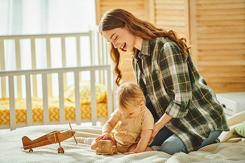 A young mother playing with her toddler daughter on a cozy bed, sharing laughter and affection.