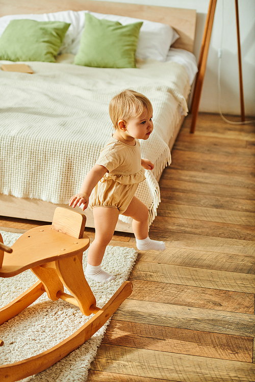 A young toddler joyfully plays on a wooden rocking toy, in a cozy home setting.