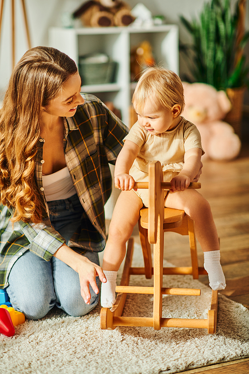 A young mother lovingly interacts with her baby daughter seated in a high chair, creating a heartwarming moment.