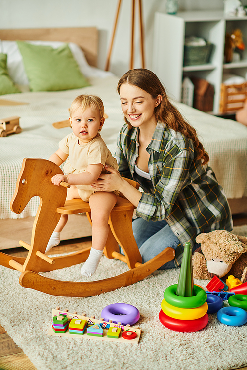 A young mother joyfully plays with her toddler daughter on a rocking horse, sharing laughter and creating cherished memories.