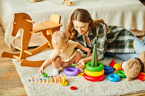 A young mother is playfully interacting with her toddler daughter on the floor, creating a heartwarming and precious moment.