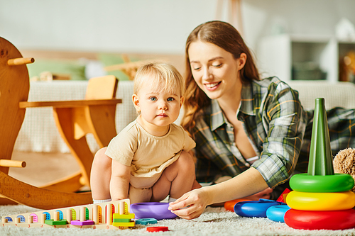 A joyful young mother interacts with her toddler daughter on the cozy floor of their home.