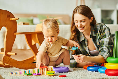 A young mother joyfully playing with her baby daughter on the cozy floor of their home.