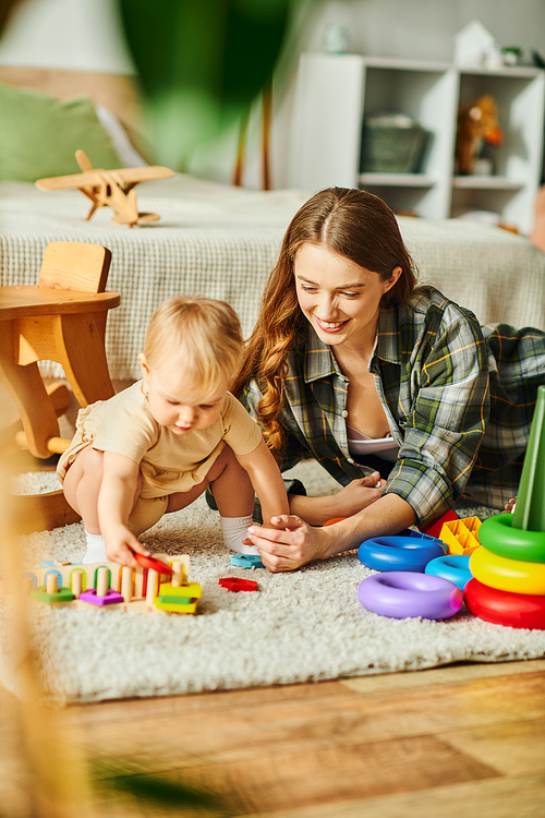 A young mother happily interacts with her toddler daughter on the floor, engaging in play and creating special moments together.