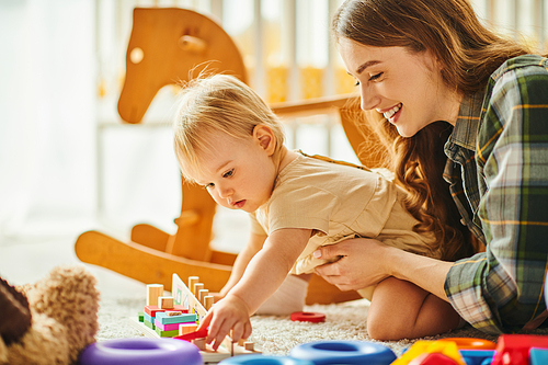 A young mother happily plays with her toddler daughter on the floor, creating cherished bonding moments.