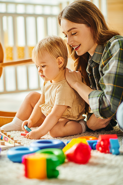 A young mother happily engages with her toddler daughter on the floor, sharing love and laughter in a tender moment.