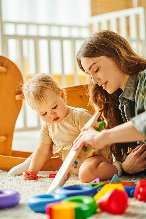 A young mother and her toddler daughter enjoy quality time together, playing with toys on the floor in a cozy home setting.