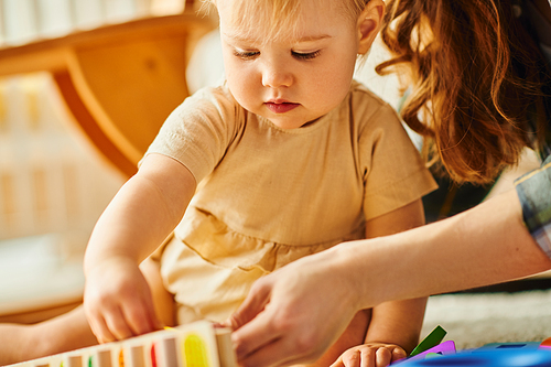 A young mother and her toddler daughter happily playing together, building structures with colorful blocks.