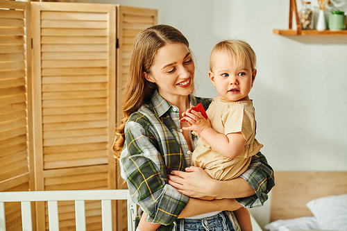 A young mother gently holding her toddler daughter in her arms, sharing a moment of love and connection at home.