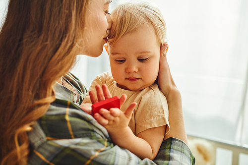 A young mother tenderly holds her small toddler daughter in her arms, sharing a moment of love and connection at home.