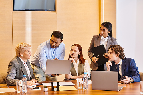 Diverse group of business professionals working on laptops at a table.