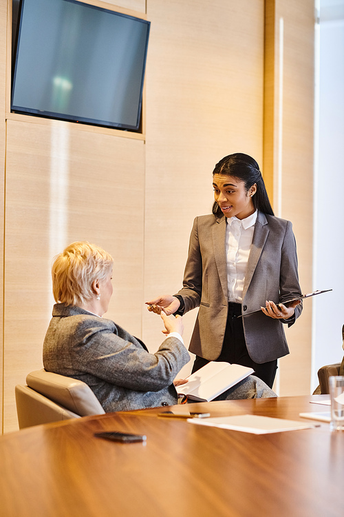 A woman confidently presents to another woman in a conference room.