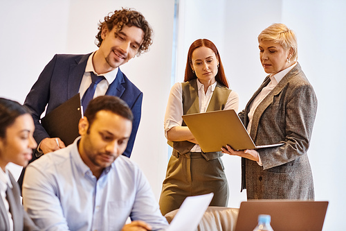 Diverse business team gather around a laptop, discussing and collaborating.