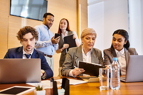 Diverse group of professionals using laptops at meeting table.