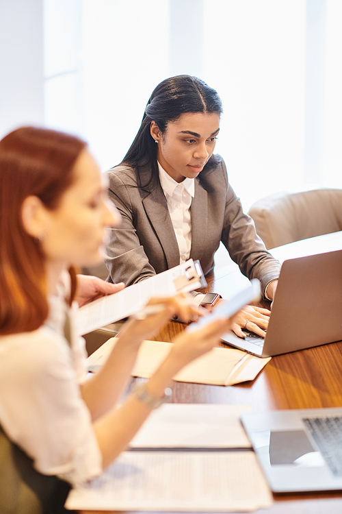 Two women of different ethnicities work intently on a laptop at a table.