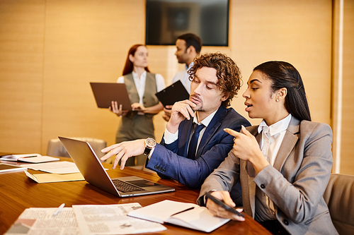 Multicultural group of business individuals working together at a table with laptops.