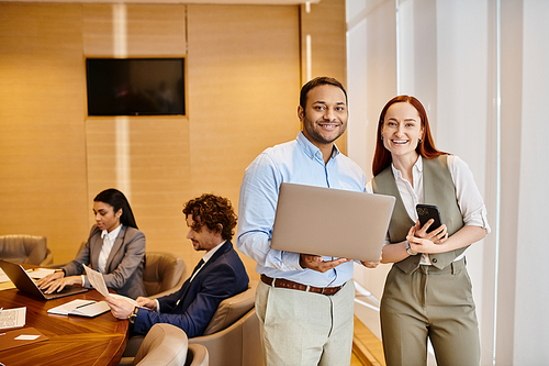 Diverse group of business professionals standing around a table with laptops, working together.