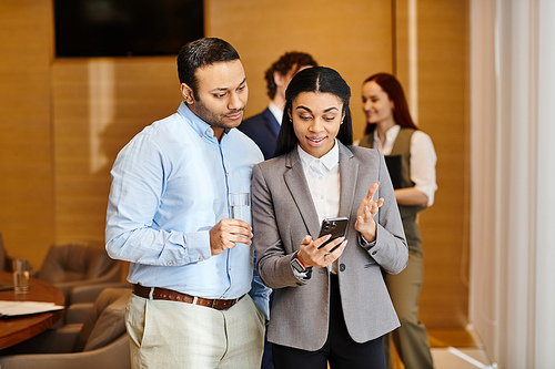 A man and woman from an interracial group of business people are engrossed in looking at a cell phone together.