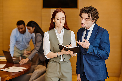 A man and woman in business attire stand by a table, brainstorming ideas together.