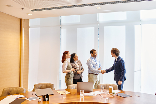 Diverse business professionals engaging in a handshake gesture inside a conference room.