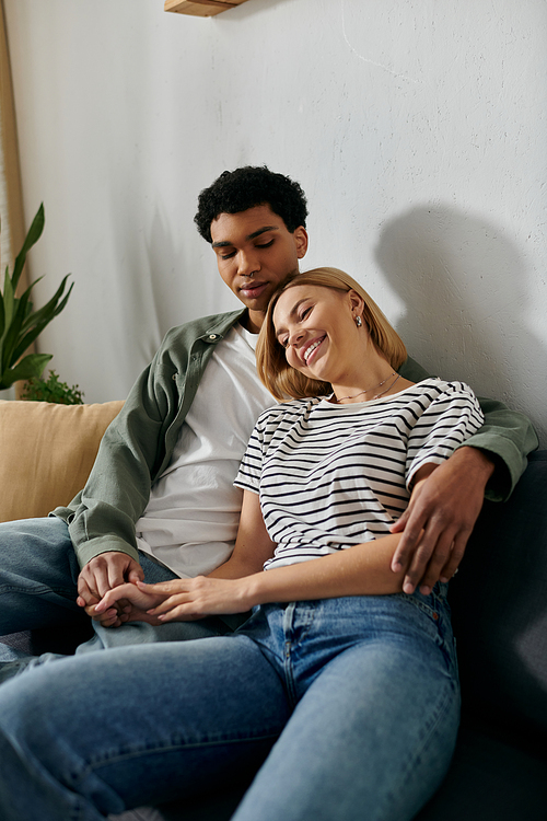 A young interracial couple relaxes on a couch in a modern apartment, enjoying each others company.