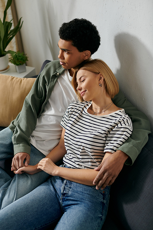 A young interracial couple relaxes on a couch in their modern apartment, enjoying a quiet moment together.