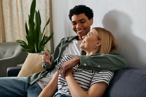 A young couple, embracing on a couch in their modern apartment, share a tender moment together.