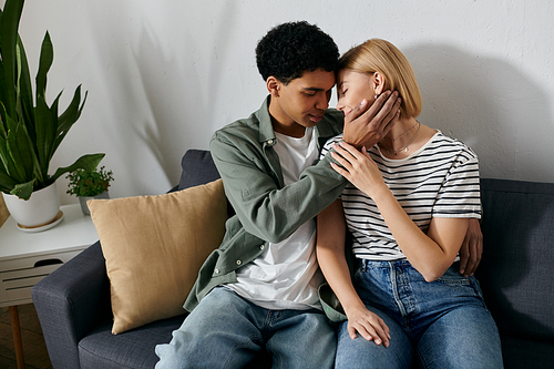 A young multicultural couple sits close together on a couch in a modern apartment, enjoying a moment of intimacy and connection.